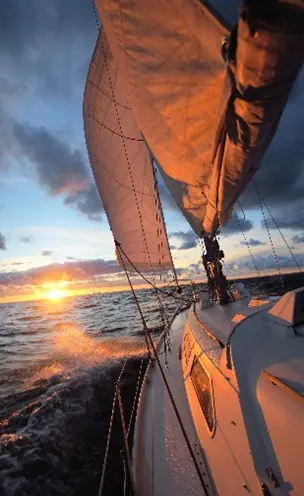 A sailboat is sailing on the ocean at sunset.