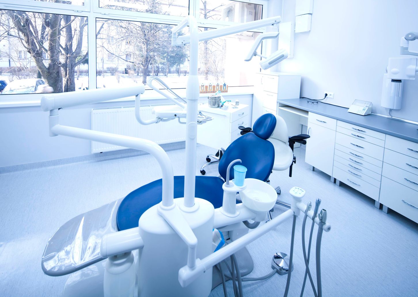 A dentist 's office with a blue chair and white walls.