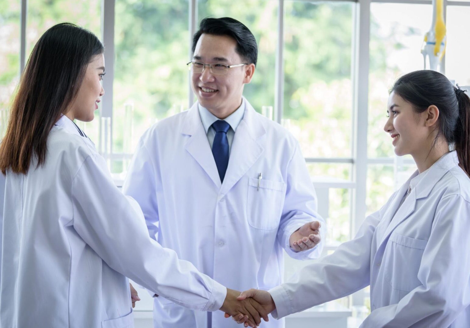 Three doctors shaking hands in front of a window.